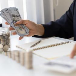 Un homme fait des calculs avec des piles de pièces et des billets dans un main